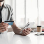 Man holding credit card and using smartphone at office