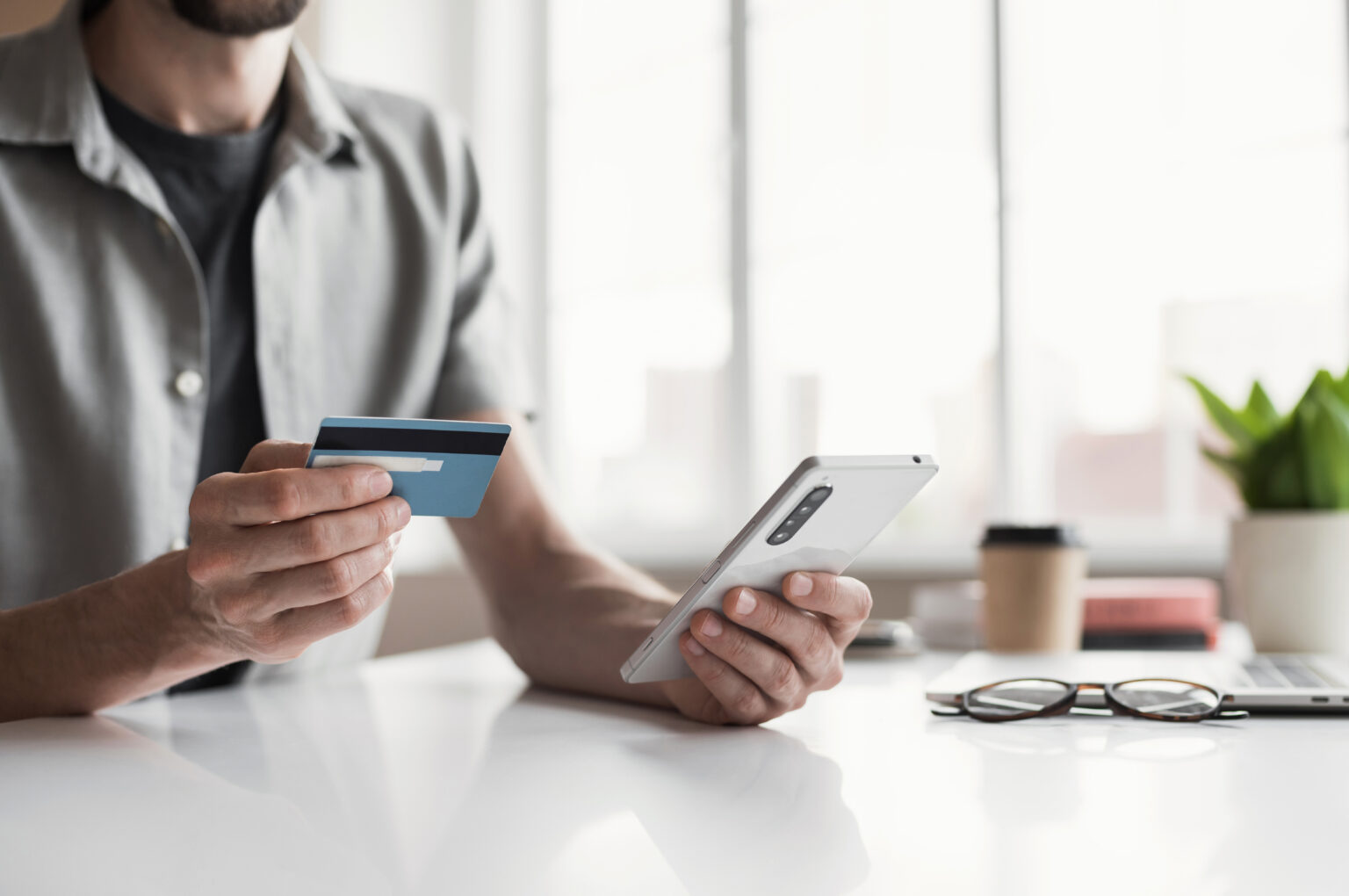 Man holding credit card and using smartphone at office