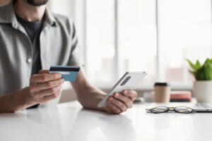 Man holding credit card and using smartphone at office